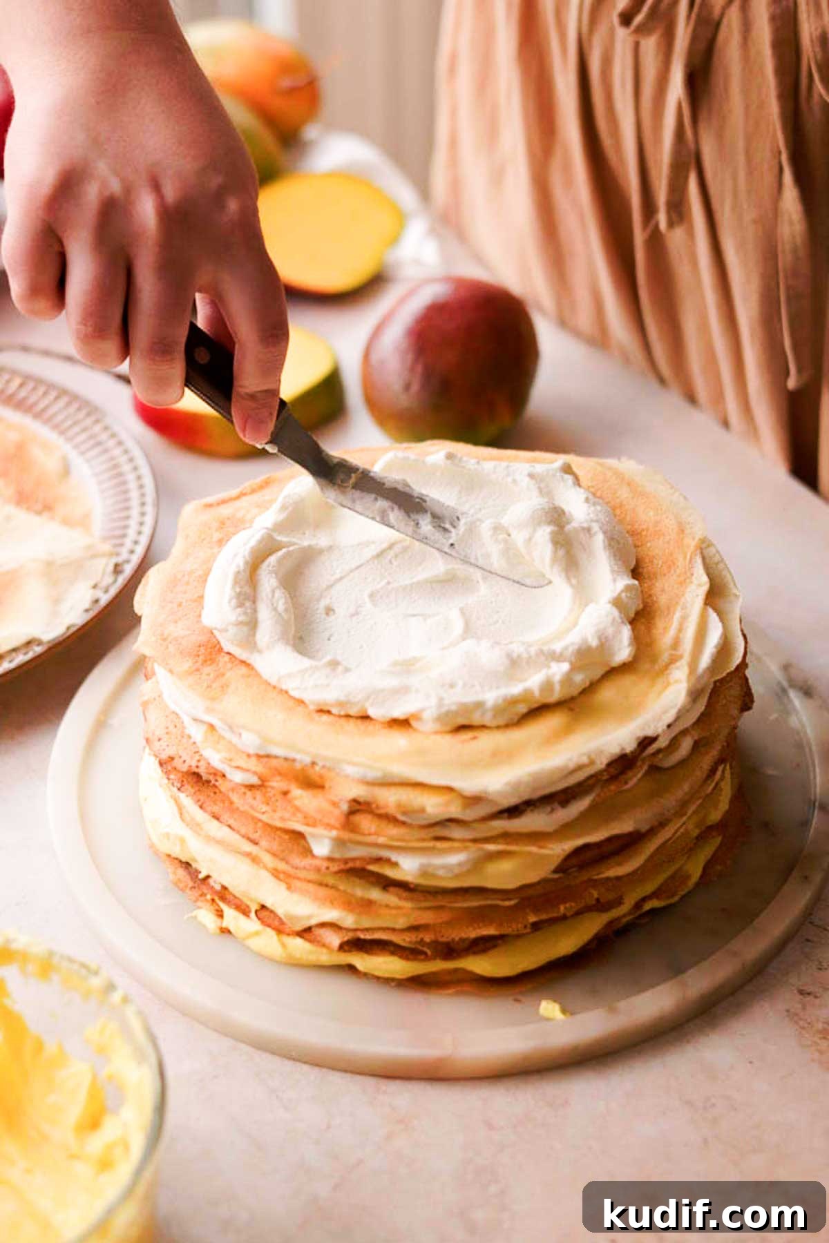 Mango Crepe Cake Recipe with Homemade Crepes Made from Scratch 16 spreading whipped cream on the layers of crepes with cream in between