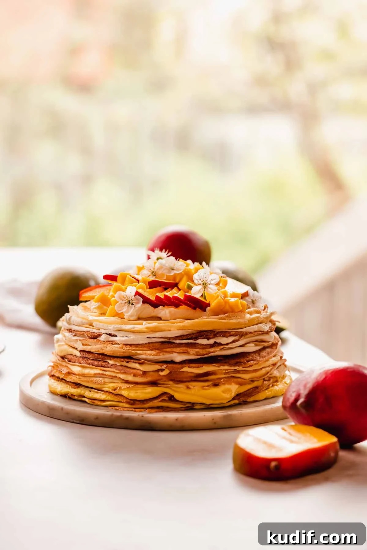 Mango Crepe Cake Recipe with Homemade Crepes Made from Scratch 18 mango crepe cake sitting on a plate with mango slices and flowers on top