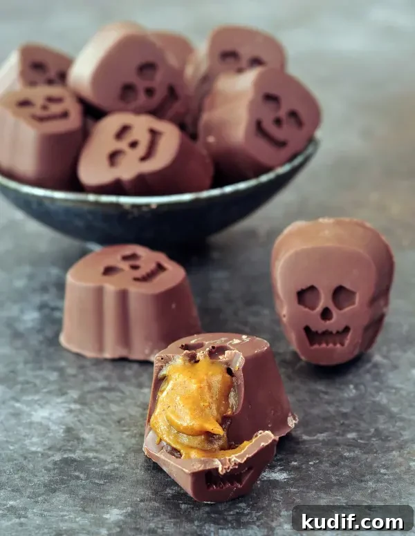 a bowl full of bite size, skull shaped Halloween chocolates stuffed with pumpkin caramel. one outside of the bowl is cut open to show the golden caramel inside.