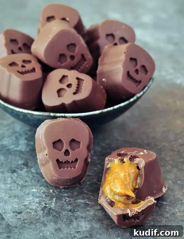a bowl full of bite size, skull shaped Halloween chocolates stuffed with pumpkin caramel. one outside of the bowl is cut open to show the golden caramel inside.