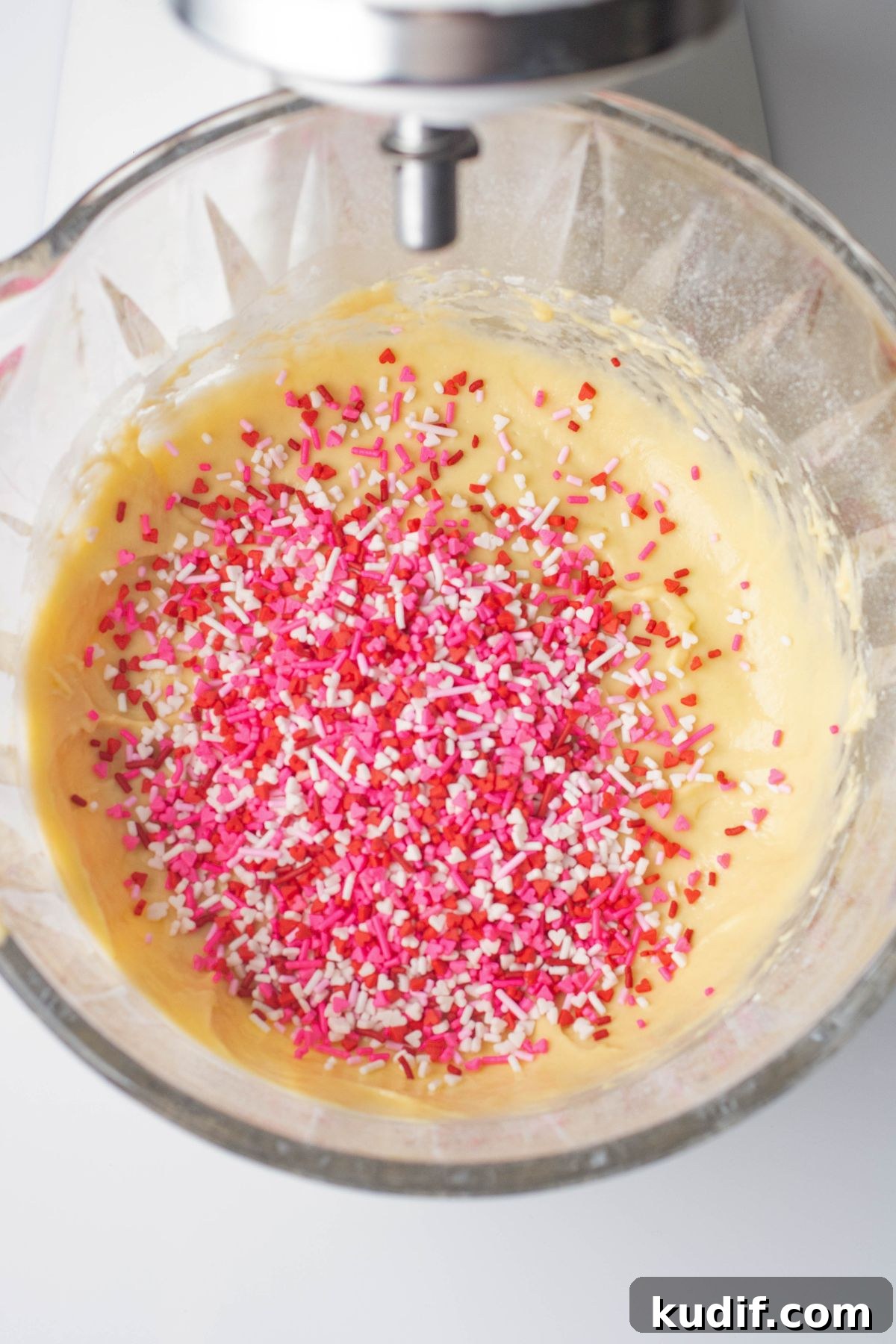 Valentine's Day sprinkles being mixed into pancake batter in a clear glass bowl. 