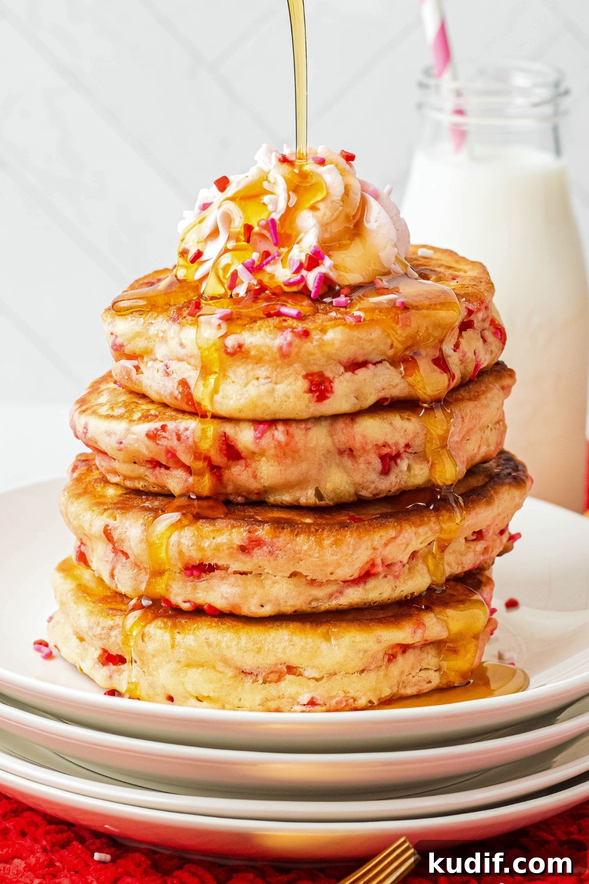 Golden fluffy Valentine's day pancakes stacked on a white plate with syrup being poured on top. 