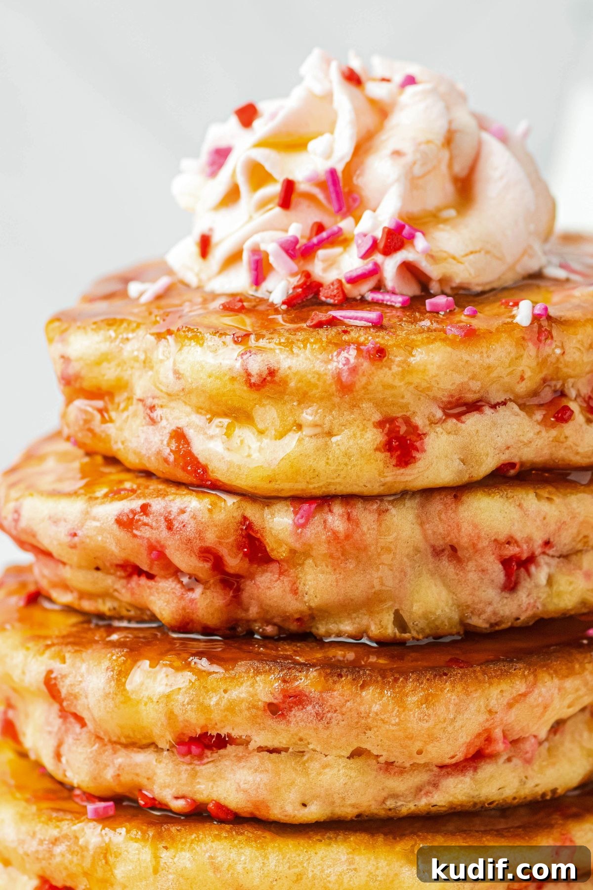 Close up image of pancakes stacked on a plate and topped with whipped cream and sprinkles. 
