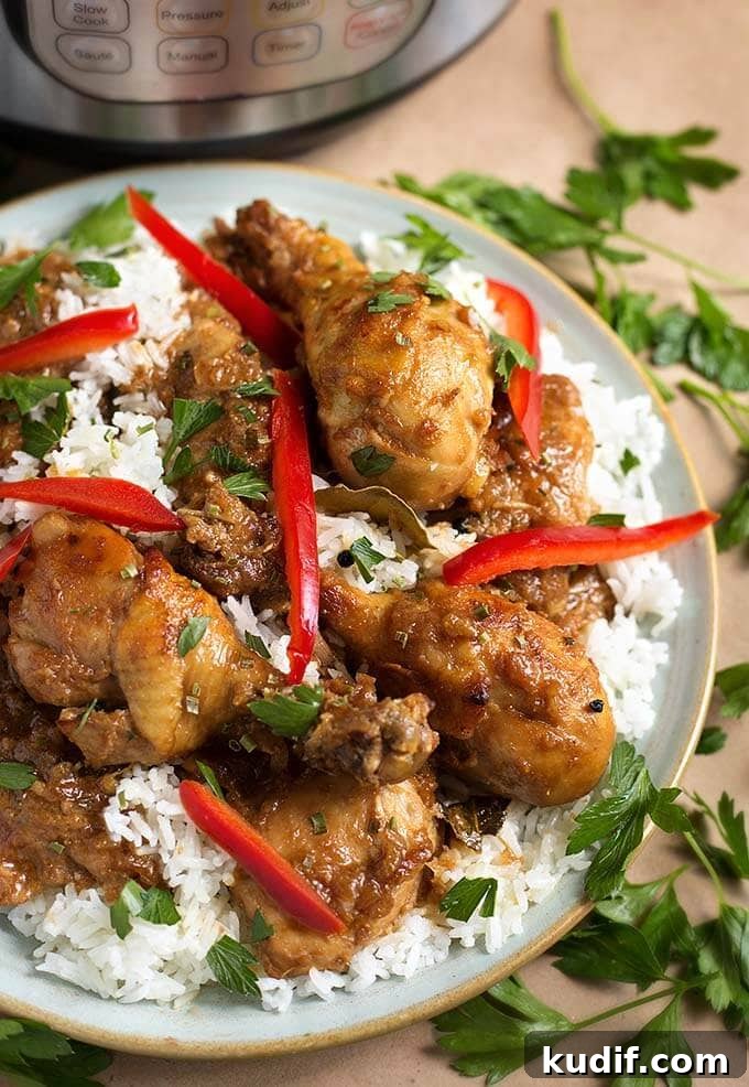 Instant Pot Filipino Chicken Adobo: Quick Authentic Recipe 2 Chicken Adobo Filipino with rice on a white plate garnished with red peppers, cilantro