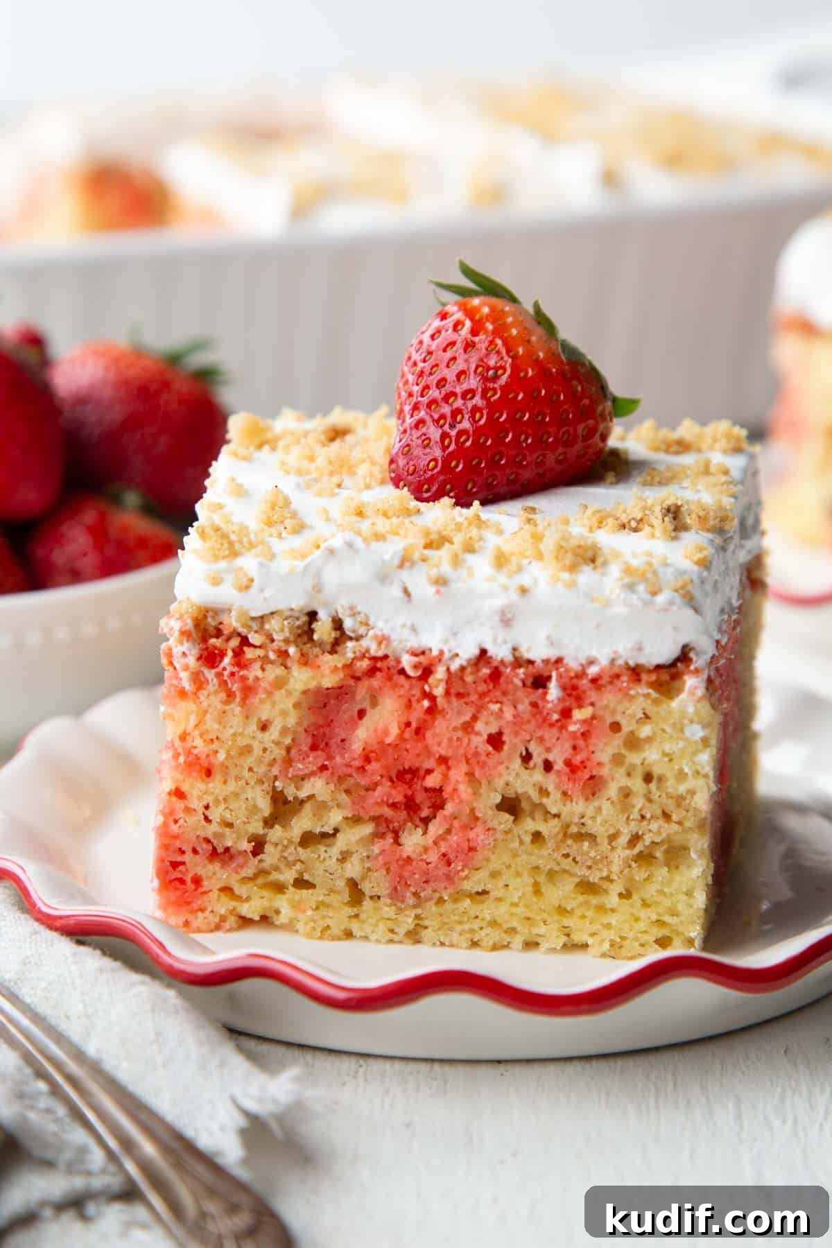 Strawberry Graham Poke Cake Recipe with Creamy Filling 2 slice of strawberry poke cake with a layer of graham cracker crumbs and nuts, topped with whipped topping and a whole strawberry.