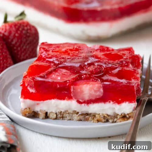 slice of a layered dessert with a pretzel crust, cream cheese filling, and strawberry gelatin on top.