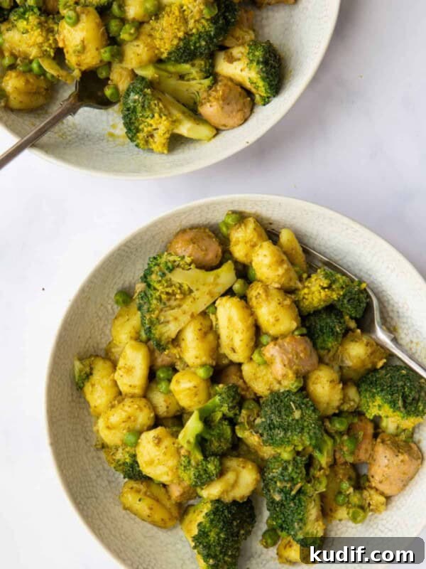 Image shows 2 bowls of Sausage Gnocchi Pasta ready to eat with forks. Bowls are displayed on a white marble background.