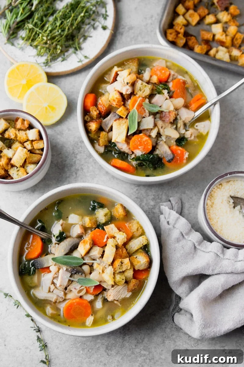 Hearty Turkey, White Bean, and Kale Soup Recipe 7 Turkey kale and bean soup in a white bowl, croutons in a white bowl, fresh lemon, croutons on a baking sheet, fresh herbs on a plate, salt and a white tea towel.