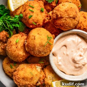 Close-up photo of potato croquettes served in a bowl with a side of aioli and lemon wedges.