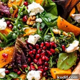 close up shot of salad greens topped with squash, pomegranate arils, nuts, and goat cheese