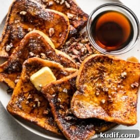 overhead shot of pumpkin french toast slices arranged on a plate with a bowl of maple syrup set next to them.
