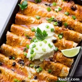 Ground Turkey Black Bean Enchiladas arranged in a gray-colored baking pan and topped with green onions, sour cream, and lime wedges.