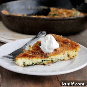 A slice of leftover turkey frittata topped with sour cream, with the skillet in the background