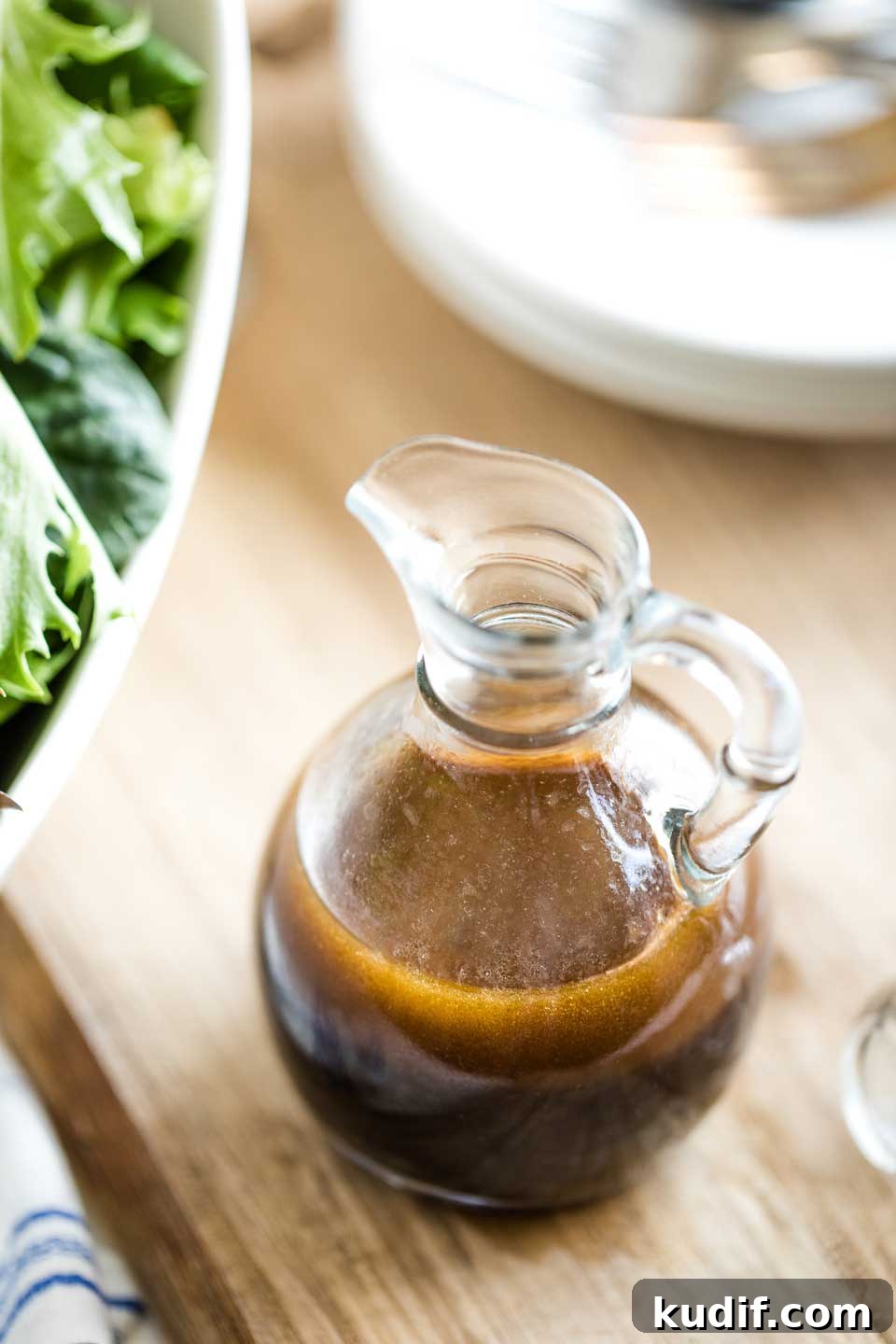 Easy Balsamic Vinaigrette Recipe salad dressing in a serving cruet next to big bowl of salad and stack of salad plates