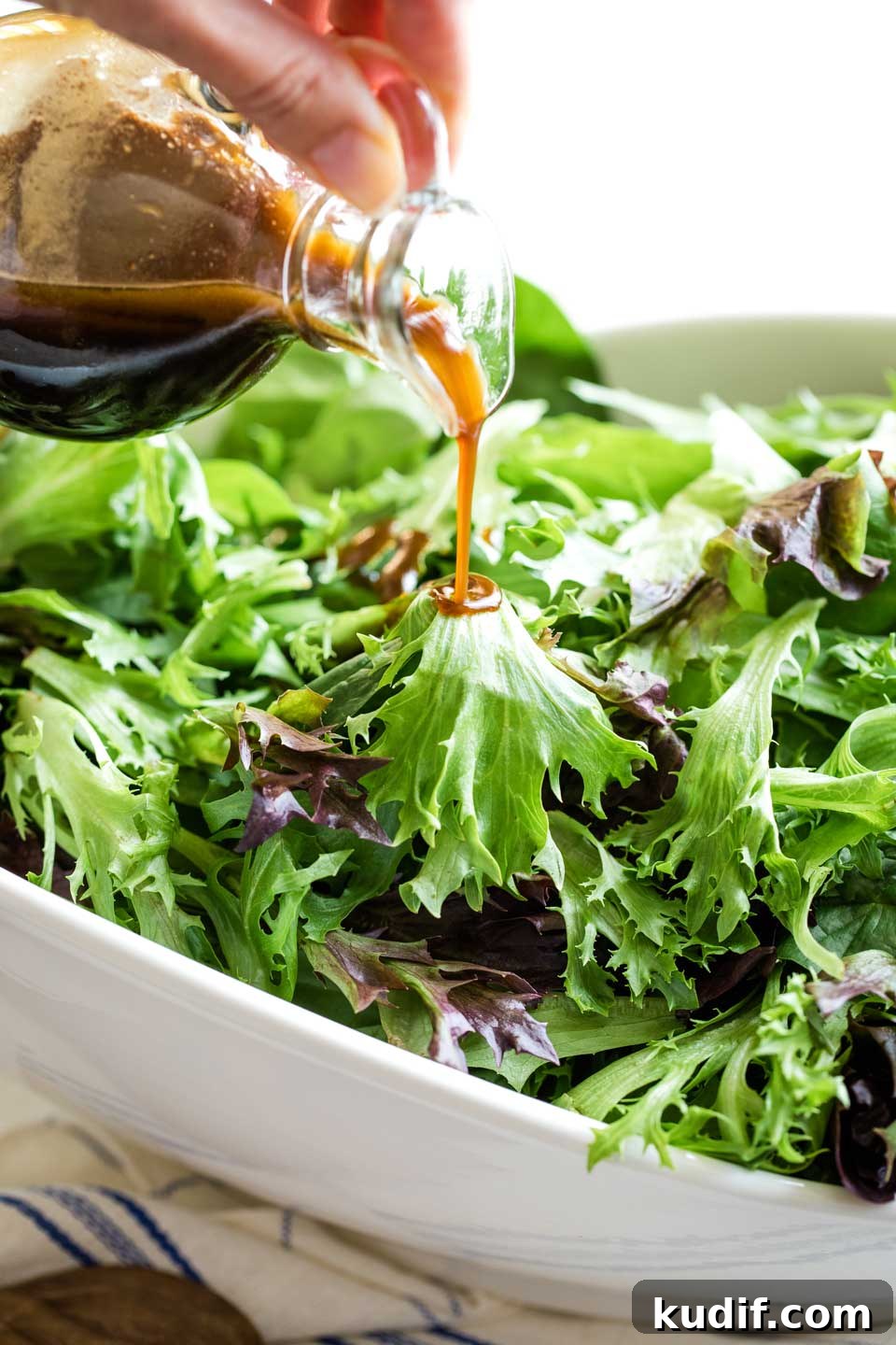 Balsamic Vinaigrette Recipe Salad Dressing salad greens in large white porcelain bowl, with cruet of balsamic vinaigrette just beginning to be poured in a slow stream over top