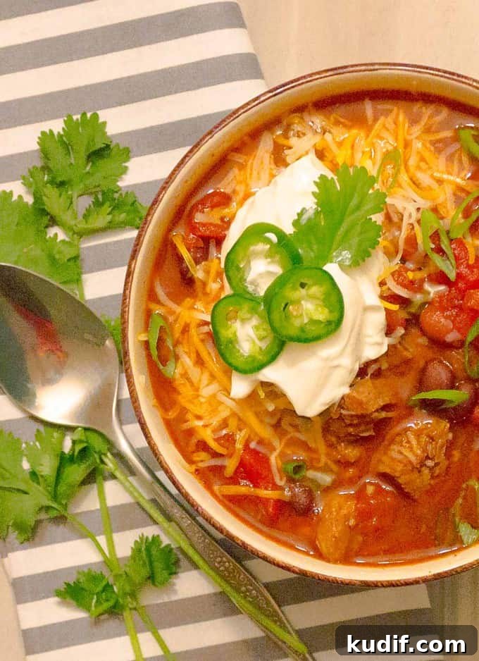 Instant Pot Red Pork Chili Recipe — Quick Pressure Cooker Meal 3 Instant Pot Pressure Cooker Red Pork Chili in a bowl with ganishings on white wood planks and a gray striped napkin.