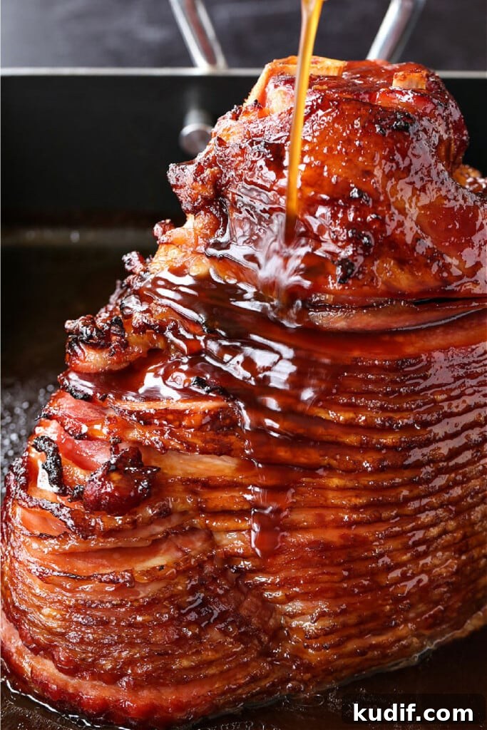 spiral sliced ham in roasting pan with glaze being poured over