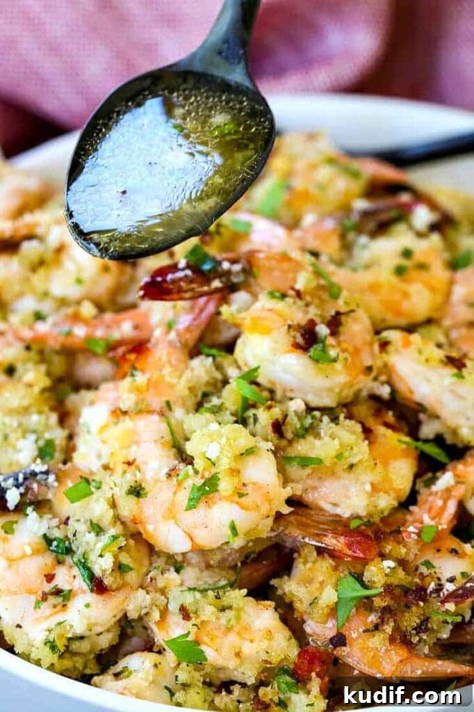 a spoon with sauce pouring over a bowl of shrimp
