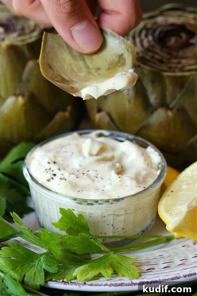 Artichoke leaf dipping into garlic aioli with lemon wedge on the side