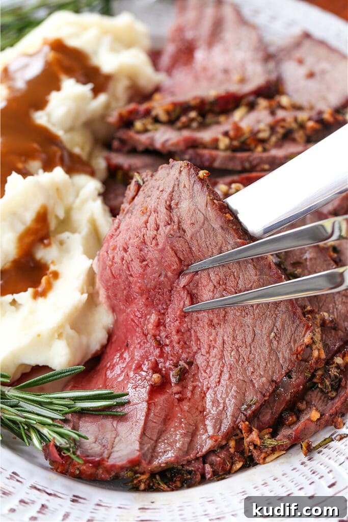 slice of rare roast beef held up with serving fork and knife