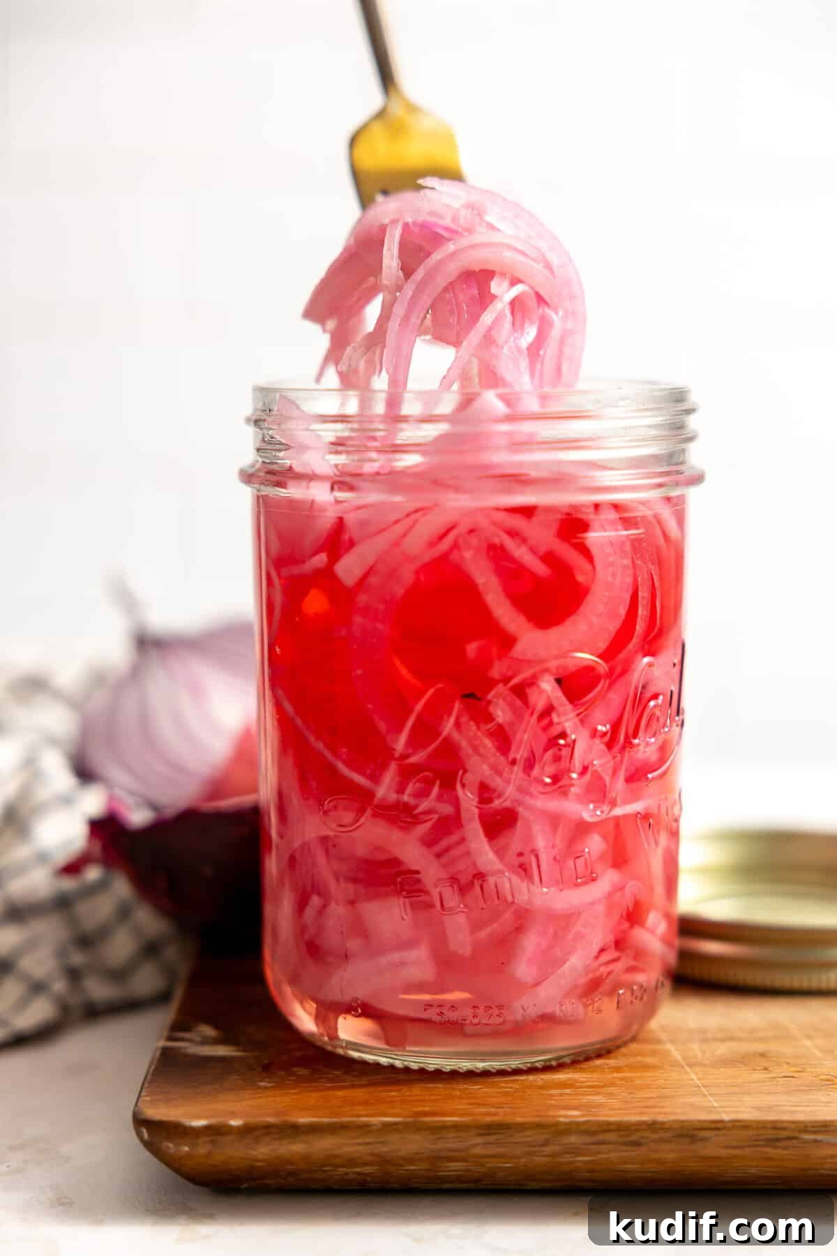 Quick Pickled Red Onions Recipe for Salads & Sandwiches 2 A jar filled with tangy and sweet pickled red onion being served up with a fork.