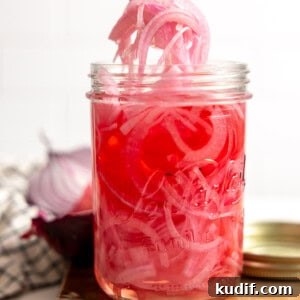 Quick Pickled Red Onions Recipe for Salads & Sandwiches 10 A jar filled with tangy and sweet pickled red onion being served up with a fork.
