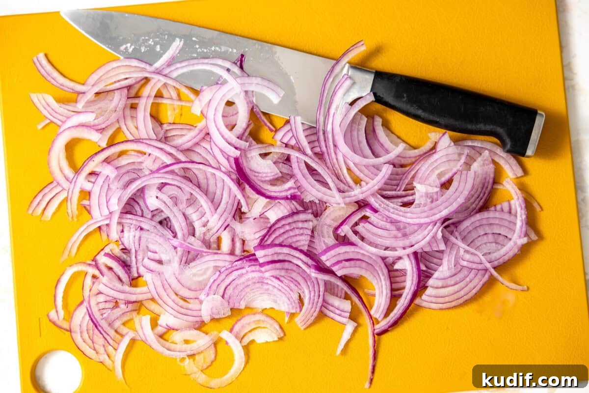Quick Pickled Red Onions Recipe for Salads & Sandwiches 6 Red onion thinly sliced on a cutting board with a black-handled knife.