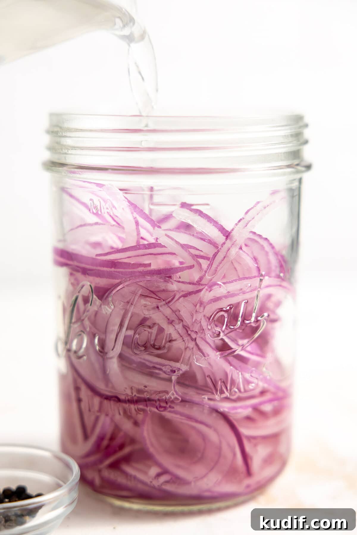 Quick Pickled Red Onions Recipe for Salads & Sandwiches 8 Pouring vinegar over thinly sliced red onions in a jar to make easy pickled onions.