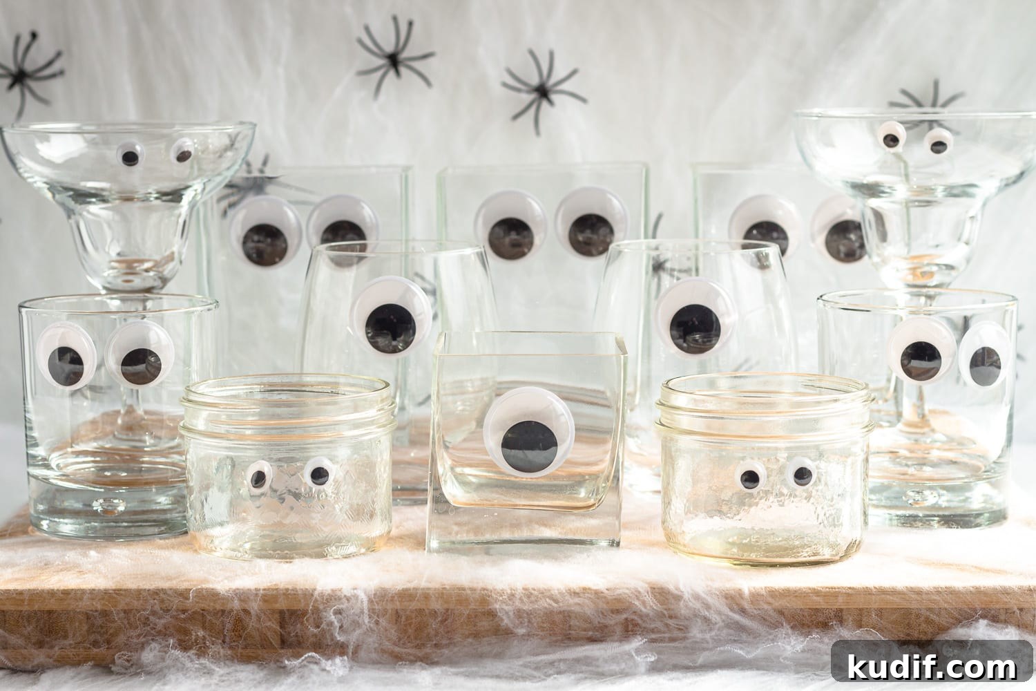 Monster-Themed Halloween Veggie Tray Ideas for Parties 5 Variety of glassware with craft googly eyes arranged on a wooden board surrounded by fake cobwebs and spiders.