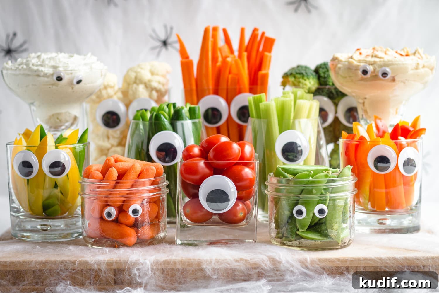 Monster-Themed Halloween Veggie Tray Ideas for Parties 6 A monster Halloween themed veggie tray featuring a variety of glassware with googly eyes filled with different veggies and dip.