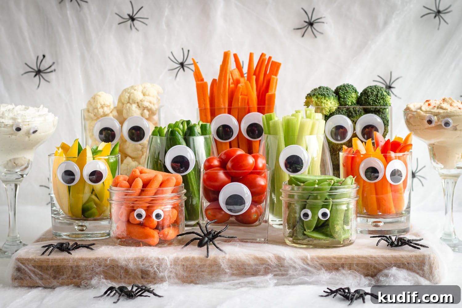 Monster-Themed Halloween Veggie Tray Ideas for Parties 8 Large Halloween themed veggie tray made using glassware and googly eyes surrounded by fake spiders and cobwebs.