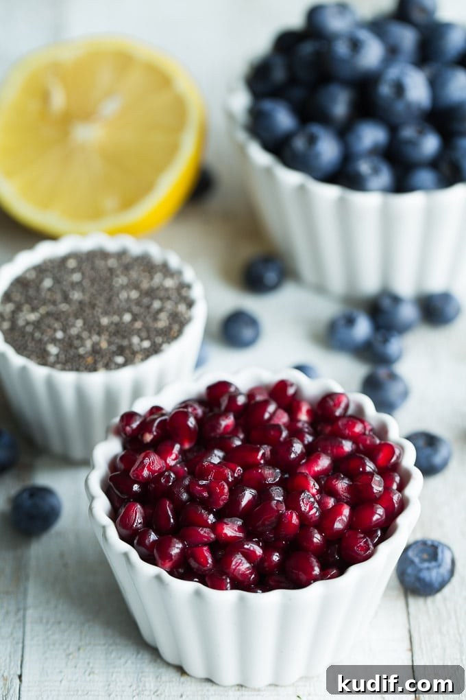 Ingredients for Blueberry Pomegranate Chia Jam in individual bowls on a wooden surface.
