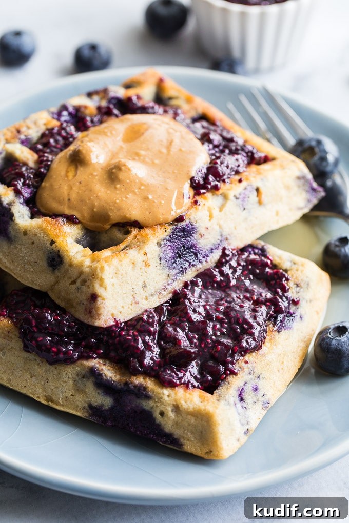 Blueberry waffles on a blue plate topped with Blueberry Pomegranate Chia Jam.