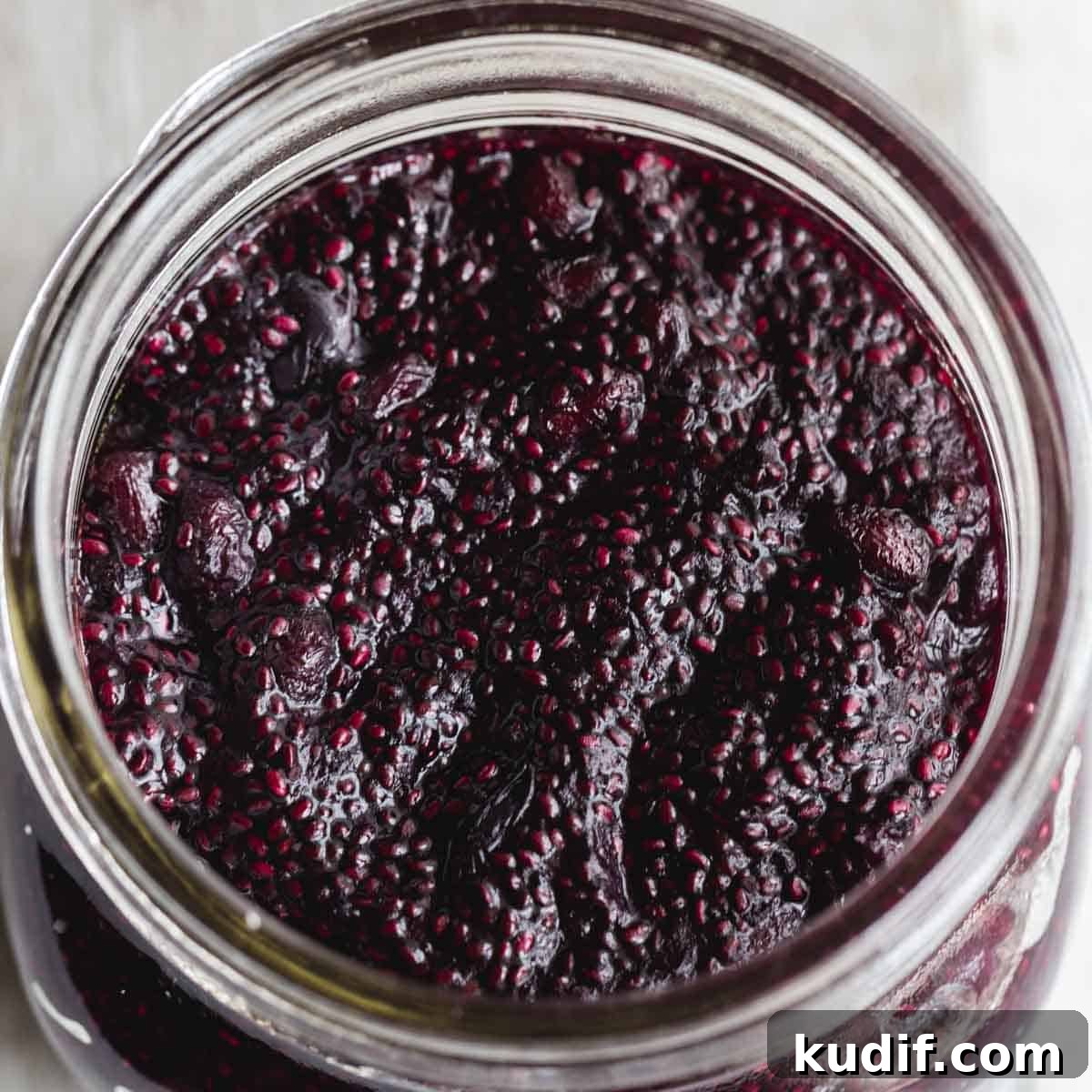 Overhead close up of blueberry chia jam in a wide mouth glass jar.