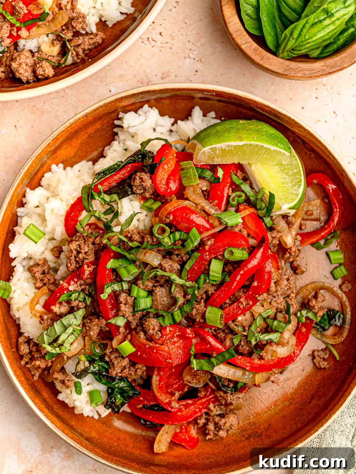 A serving of Thai basil beef with red bell peppers, onions, and fresh basil over white rice.