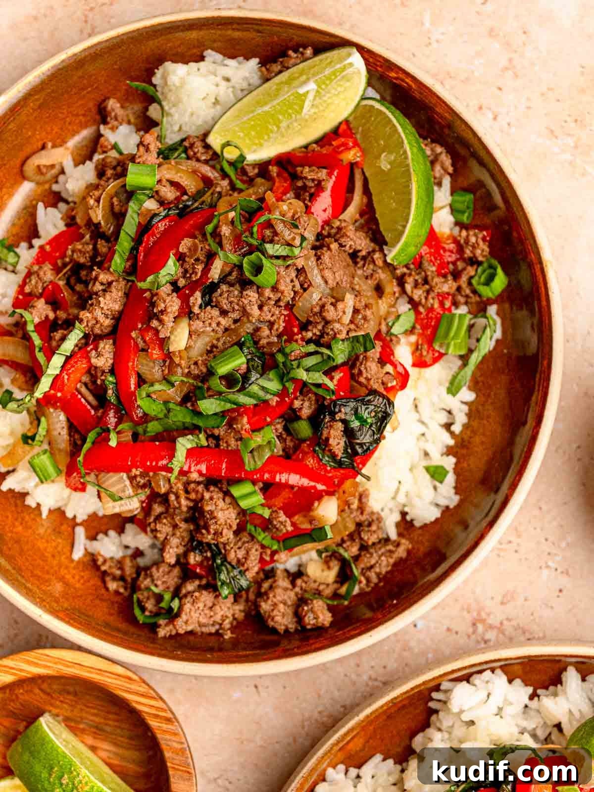 Thai basil beef with red bell peppers, onions, fresh basil, and green onions over white rice, with a lime wedge on the side.