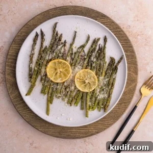 20-Minute Garlic Lemon Asparagus Recipe for Quick Weeknight Sides 9 Overhead shot of Garlic Lemon Asparagus on a white plate with two slices of lemon on top