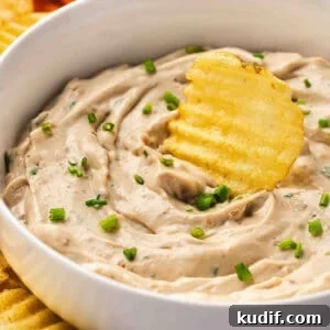 Creamy French Onion Dip Recipe for Parties and Snacks 3 French onion dip in a white bowl with chives, served with crinkle-cut potato chips and fresh vegetable sticks