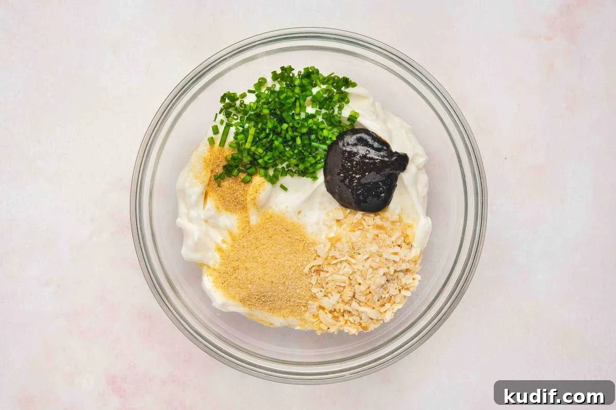 Creamy French Onion Dip Recipe for Parties and Snacks 5 French onion dip ingredients in a glass bowl, including sour cream, dried onion flakes, chives, seasonings, and beef bouillon paste
