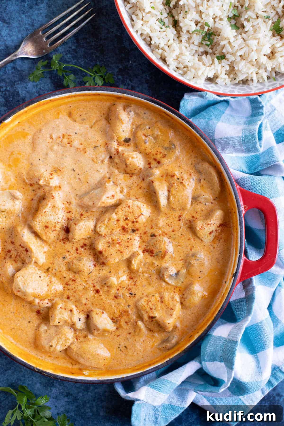 Creamy Chicken and Mushroom Stroganoff Recipe 2 Chicken and mushroom stroganoff in a red pan with a bowl of rice on the side.