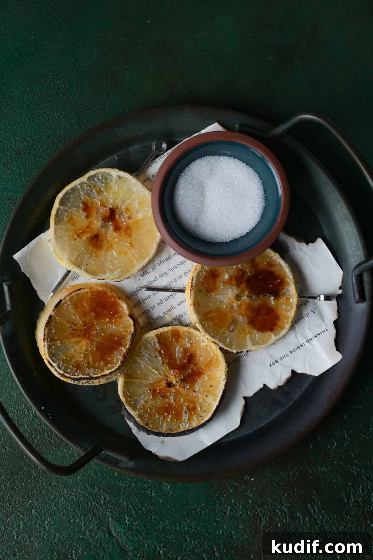 Lemon brûlée slices on a black tray with sugar.