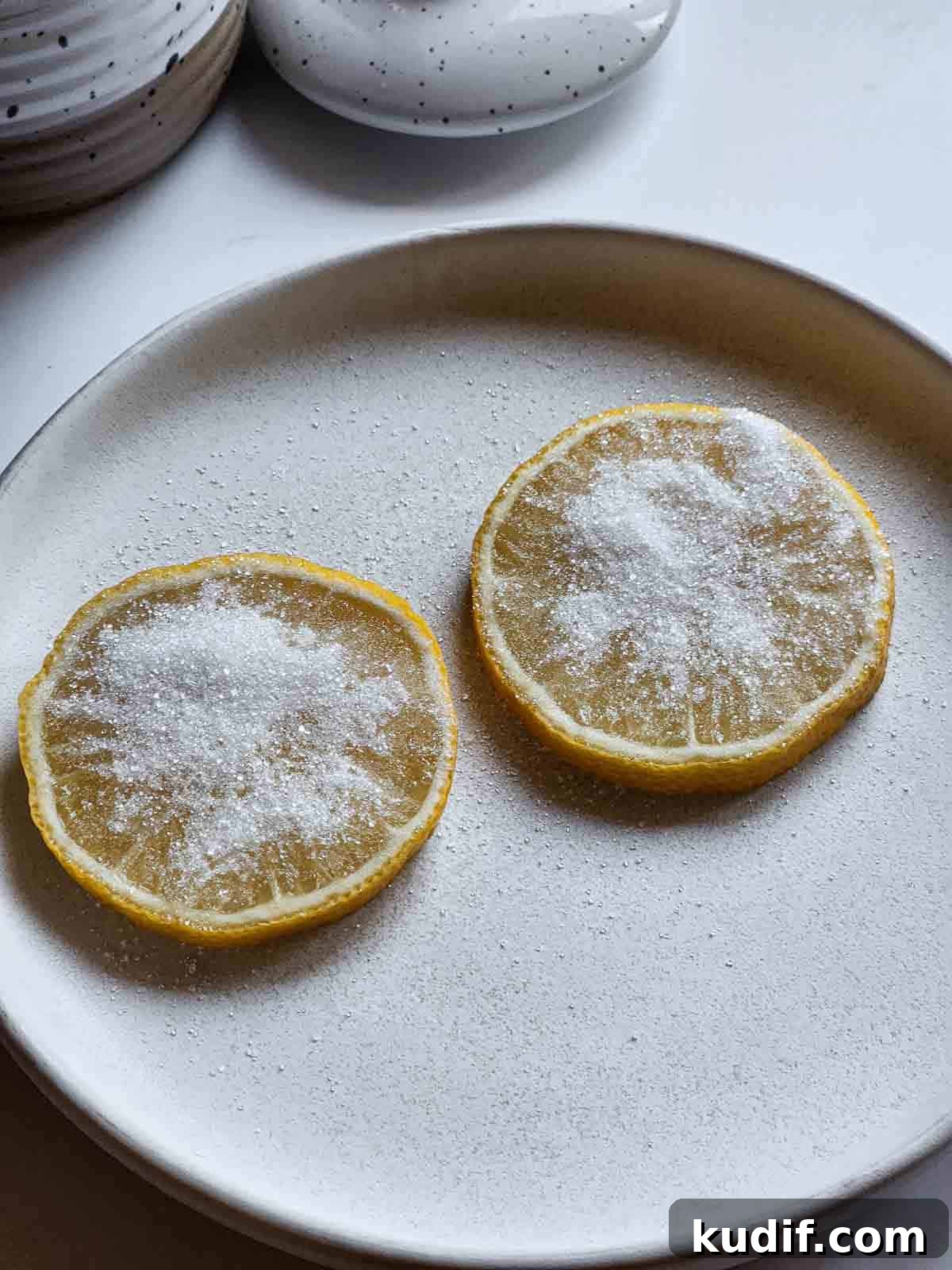 Two lemon slices with sugar on them on a white plate.