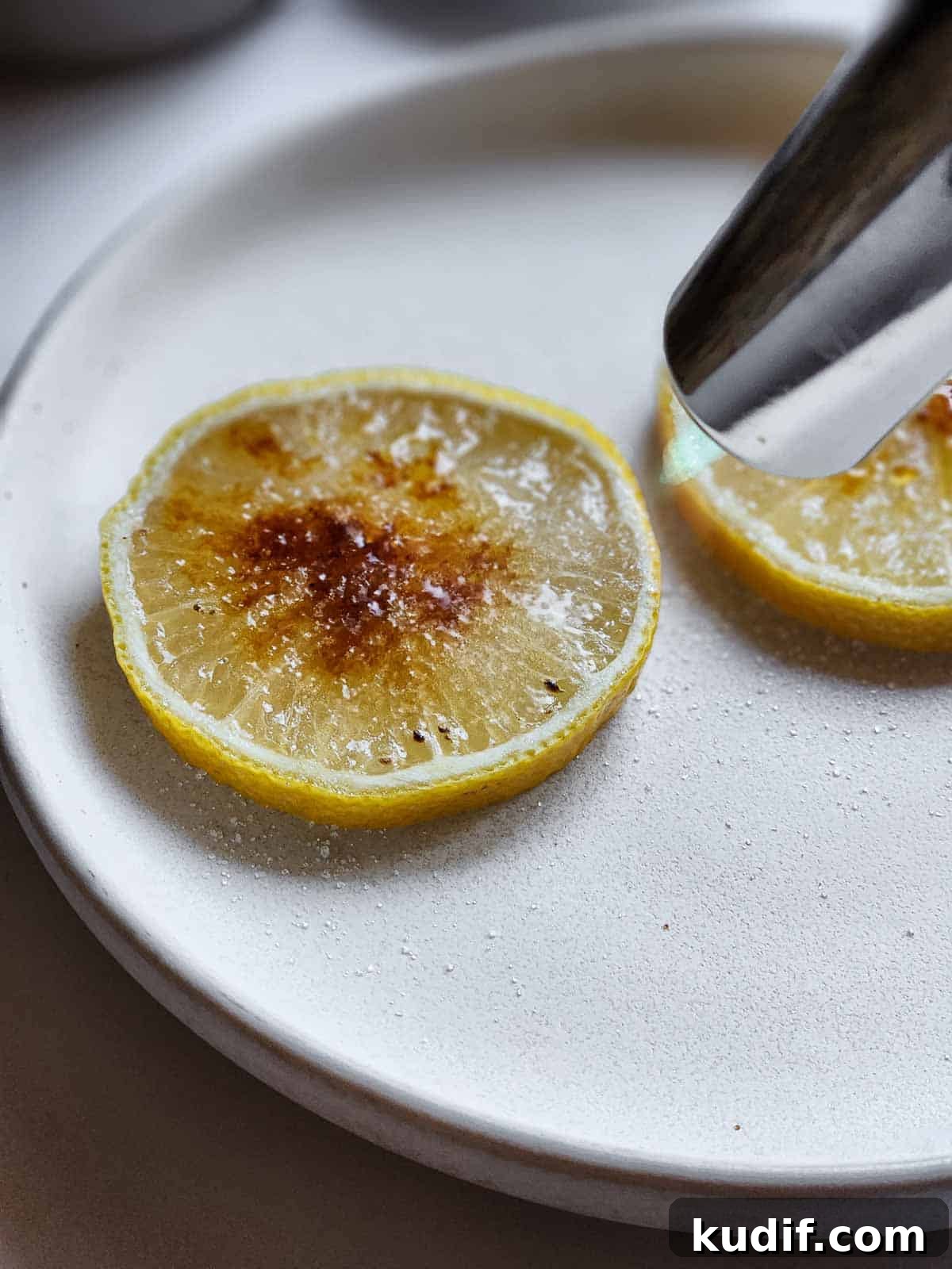 Sugared lemon slices with a kitchen torch pointed at them getting torched.