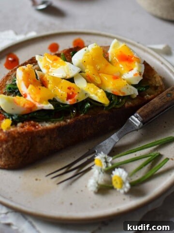 Close-up on smashed egg on toast with spinach and chili oil on a brown plate.