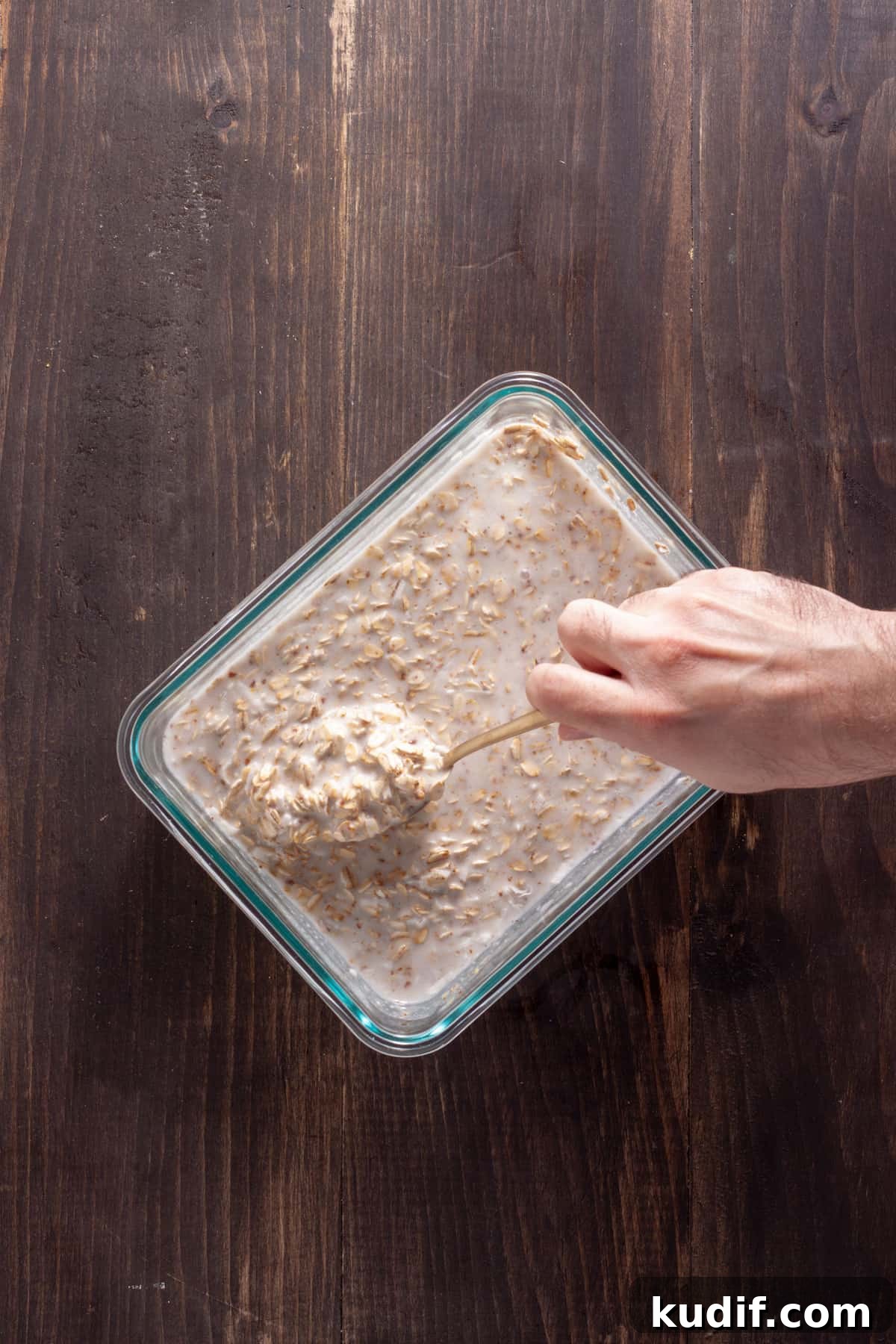 Overnight oats with coconut milk getting stirred together in a glass container.