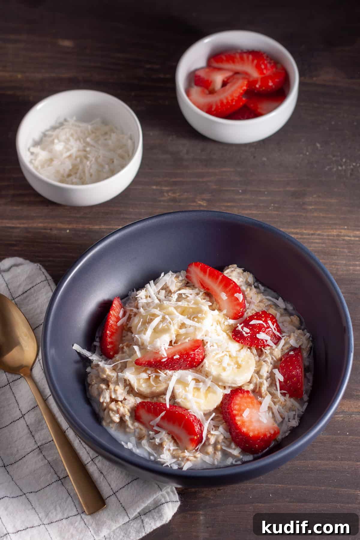 A bowl of overnight oats made with coconut milk in a blue bowl topped with shredded coconut, berries and banana slices.