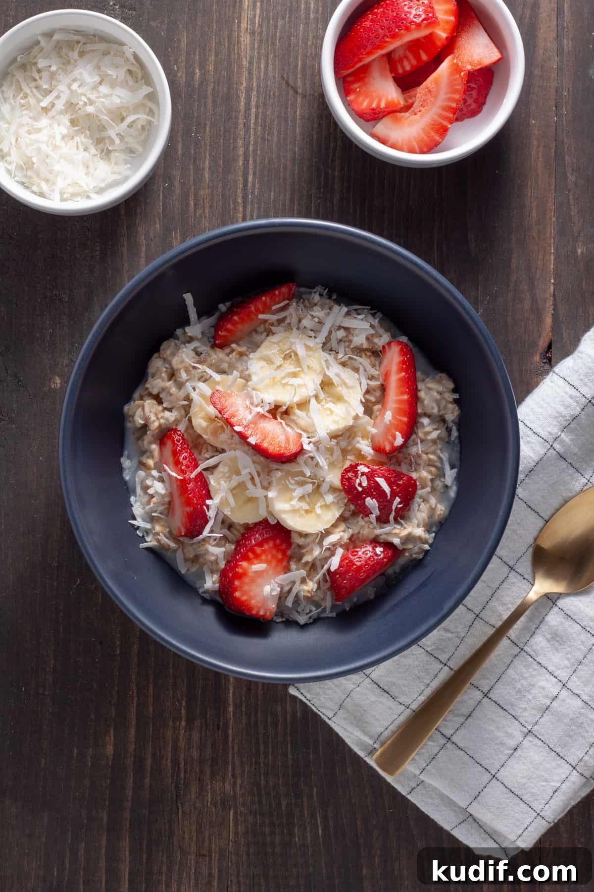 A serving of coconut overnight oats in a blue bowl topped with strawberries, shredded coconut and bananas. 