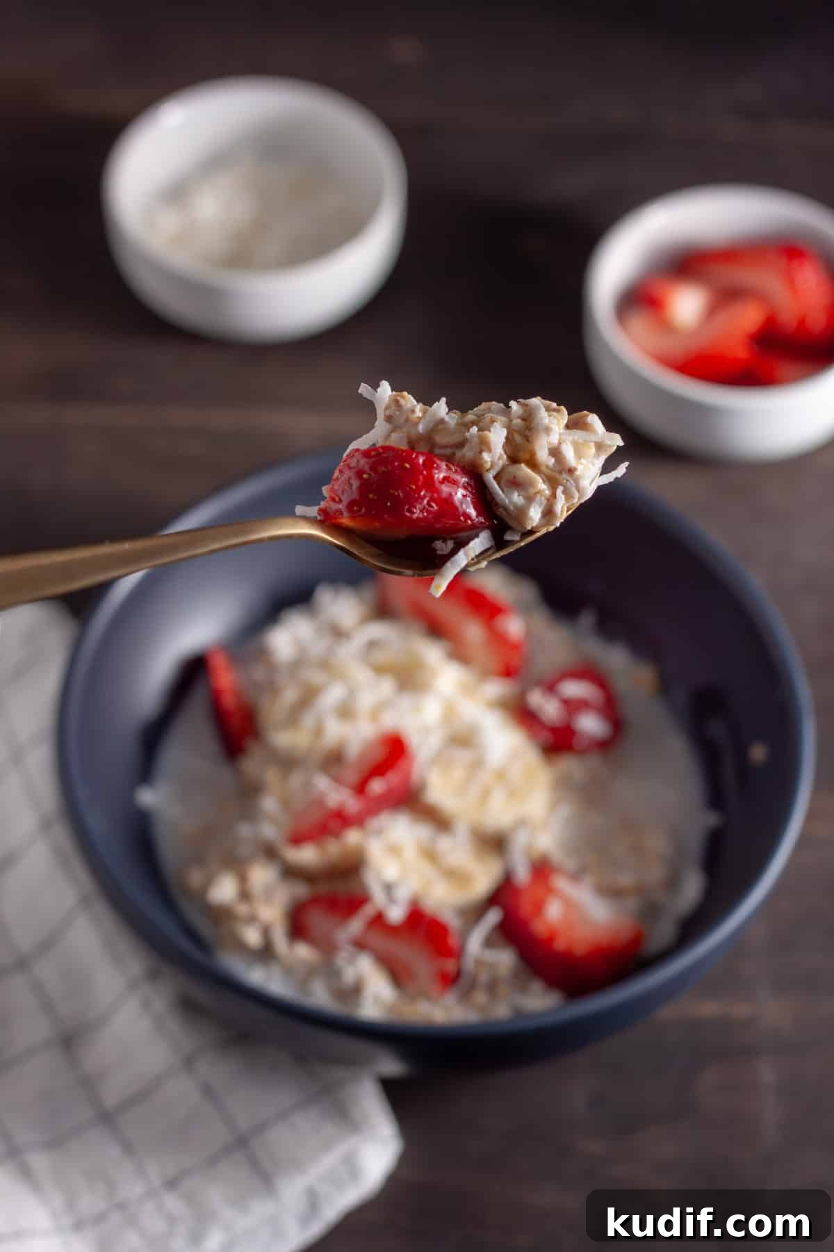 A spoonful of coconut overnight oats above a bowl of the oats with strawberries, bananas and shredded coconut.