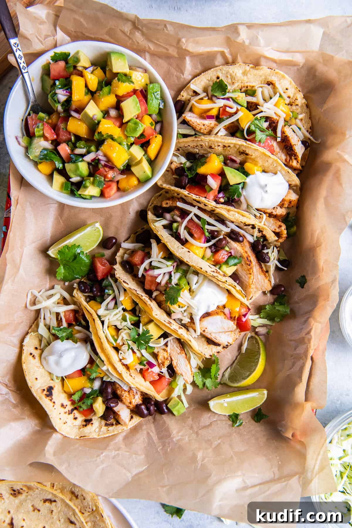 A top down shot of chicken tacos with mango salsa on parchment paper.