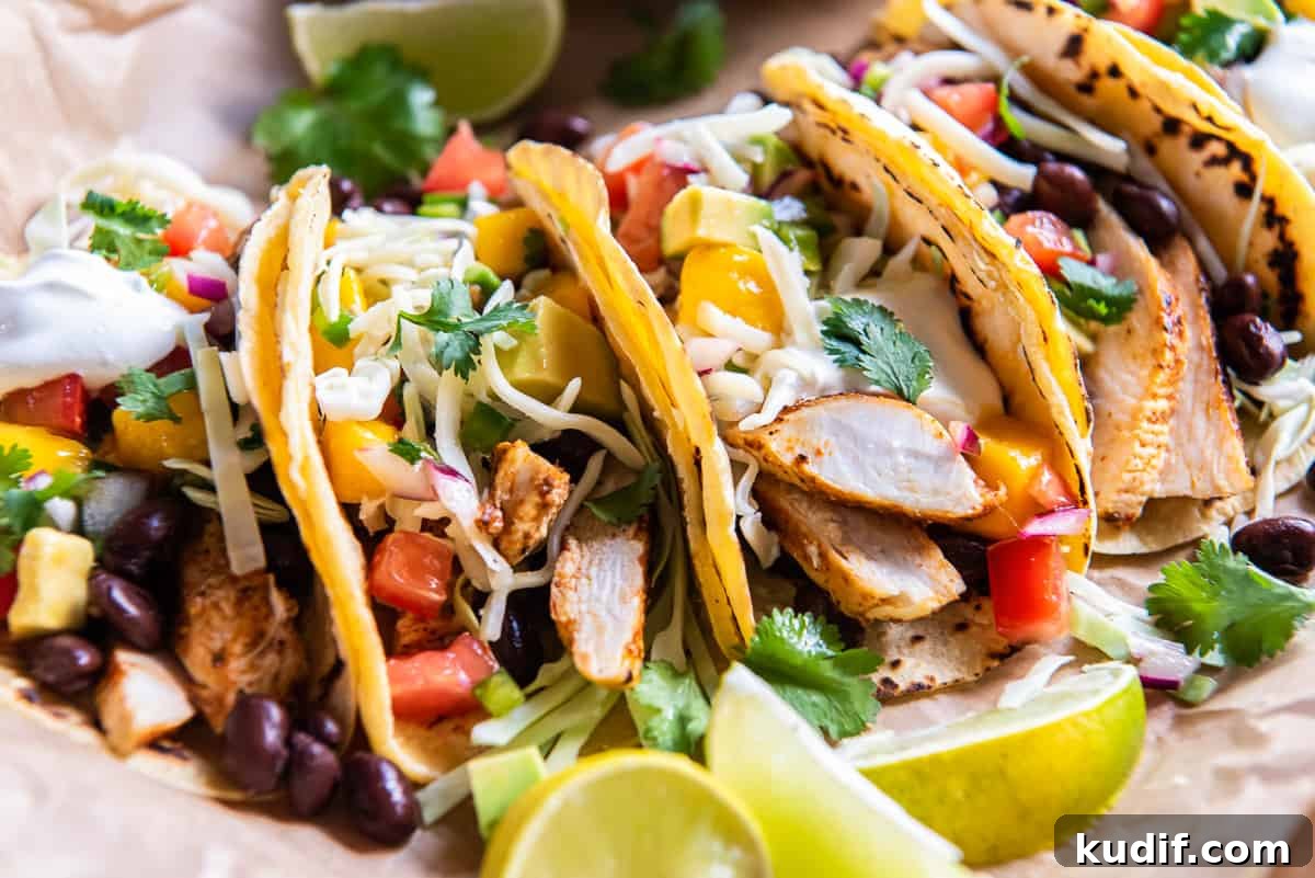 A side view of chicken tacos topped with mango salsa and cheese.